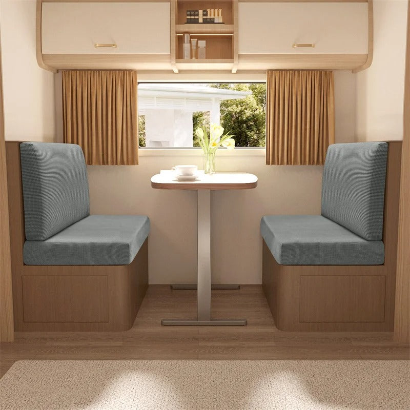 Wohnmobil-Sitzgruppe mit grauen Polstern, Holztisch, Vorhängen, ideal für Campingreisen.