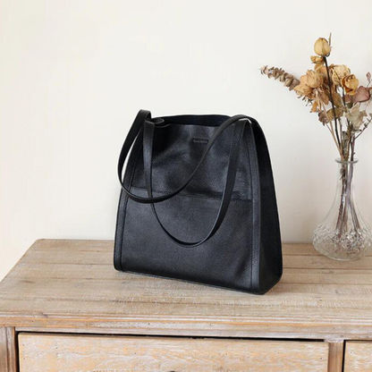 Schwarze Ledertasche auf Holztisch, elegante Damenhandtasche, minimalistisches Design.