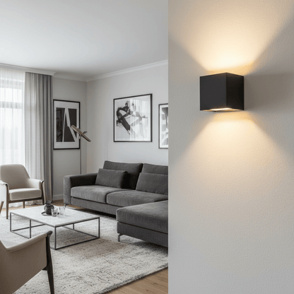 Svart kubformad vägglampa på en strukturerad vägg, med varmt ljus uppåt och nedåt, och en grå soffgrupp i bakgrunden. 2