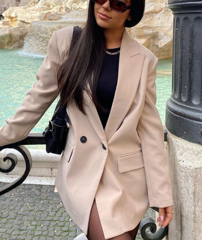 Frau in beigem Blazer vor Brunnen, schwarze Sonnenbrille, modisch, stilvoll, elegantes Outfit.