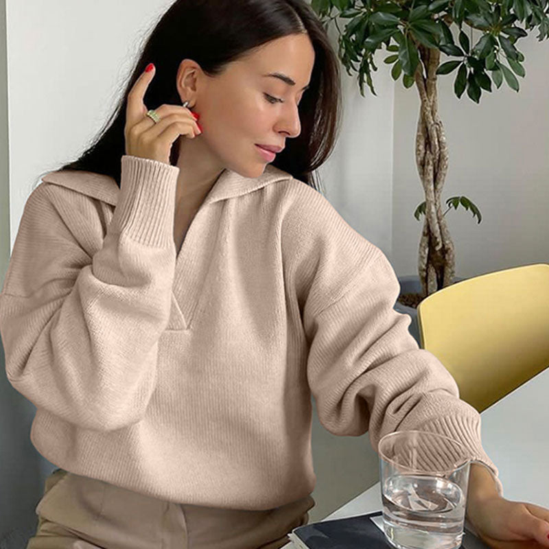 Frau in beigem Pullover, sitzt am Tisch mit Glas Wasser, moderne Inneneinrichtung, gemütlich.