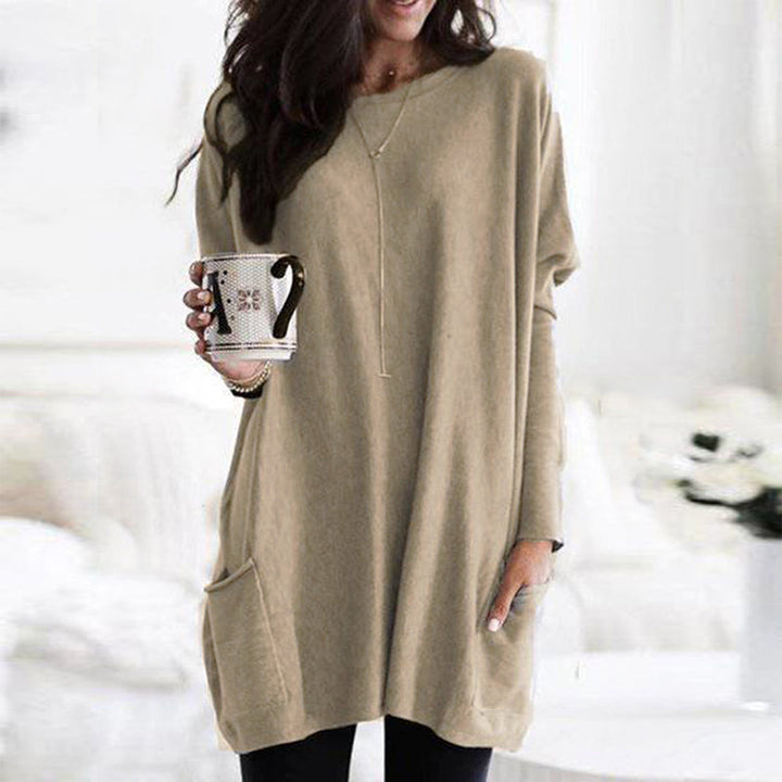 Frau in beigem Oversize-Pullover mit Kaffeetasse, gemütliche Herbstmode, Wohnzimmer.