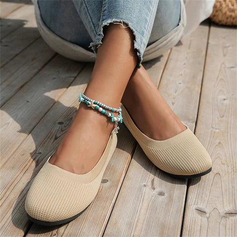 Beige Damen-Ballerinas aus Stoff, lässig, mit blauer Perlenkette, auf Holzterrasse.