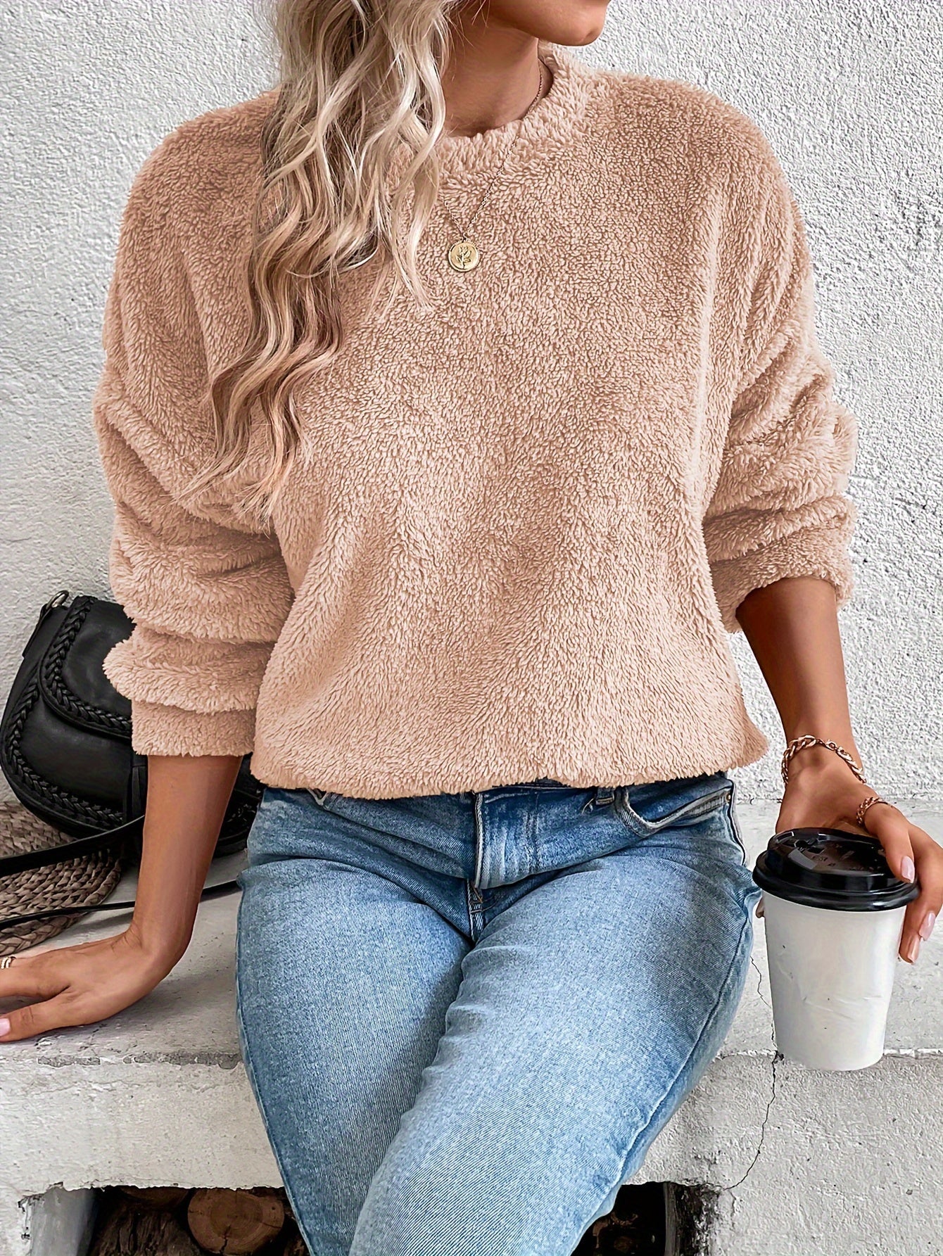 Frau in beigem Fleece-Pullover, blaue Jeans, hält Kaffeebecher, modisch, gemütlich.