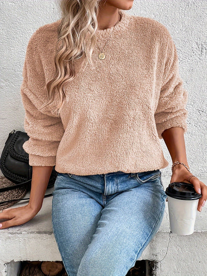 Frau in beigem Fleece-Pullover, blaue Jeans, hält Kaffeebecher, modisch, gemütlich.