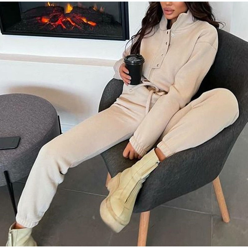 Frau in beigem Jogginganzug, sitzt auf Stuhl, hält Kaffeetasse, gemütliche Wintermode.
