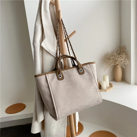 Beige Damenhandtasche aus Leinen mit braunen Ledergriffen, hängend an Holzständer.