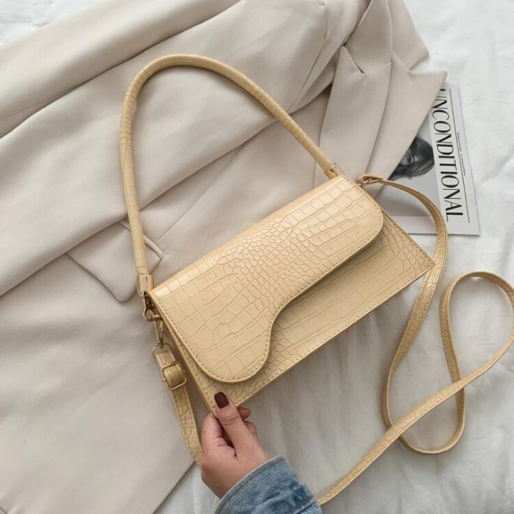 Beige Krokodilleder-Handtasche mit Schulterriemen auf cremefarbenem Blazer, stilvoll und elegant.