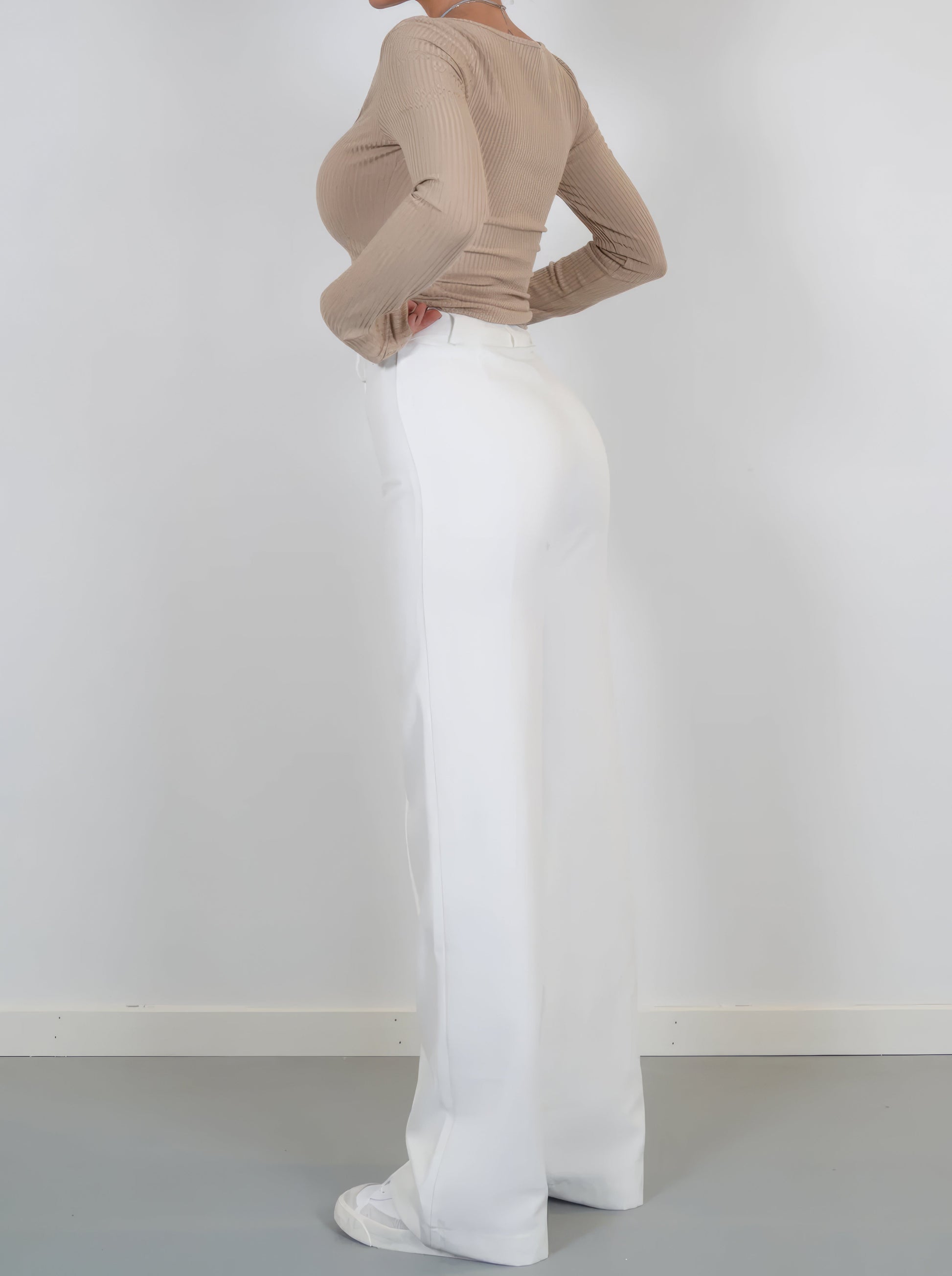 Frau in beigem Langarmshirt und weißer Hose, seitlich, Mode, Damenbekleidung, elegant.