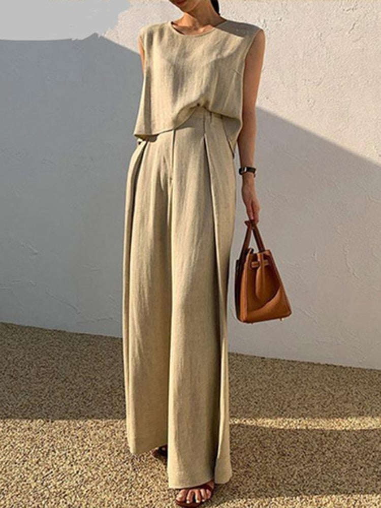 Damen Leinen Jumpsuit Beige, ärmellos, Sommermode, elegant, mit brauner Handtasche.