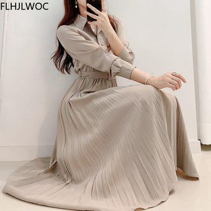 Frau in beigem, plissiertem Maxikleid, sitzt auf Boden, elegante Mode, langärmeliges Design.