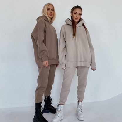 Zwei Frauen in beigen Oversize-Hoodies und Jogginghosen, eine mit schwarzen, eine mit weißen Stiefeln.