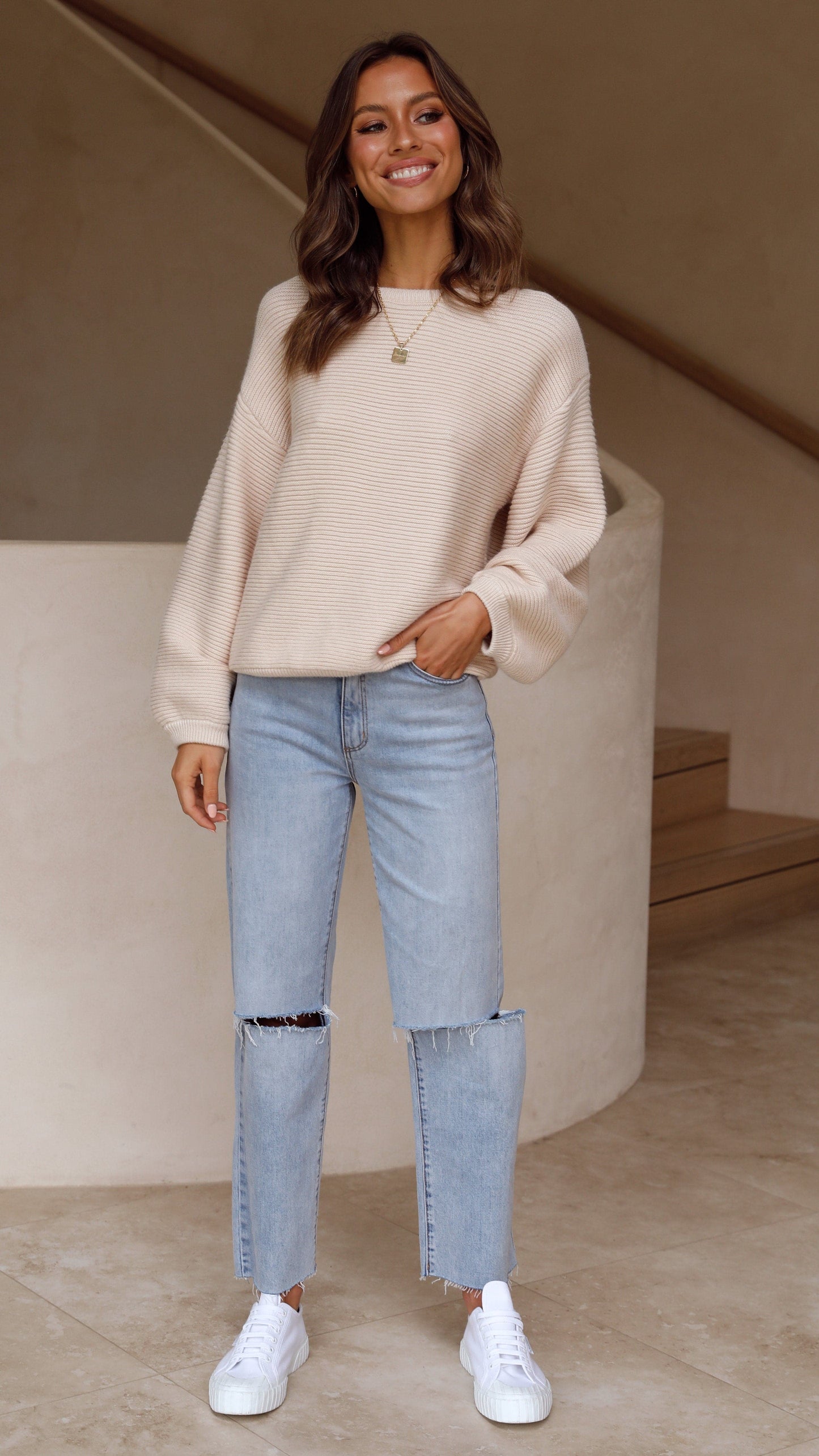 Frau in beigem Pullover und blauer Jeans, lächelnd, modisch, lässiger Stil, weiße Sneaker.