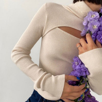 Frau in cremefarbenem Strickpullover mit Cut-Out, hält lila Blumenstrauß, modisch, elegant.