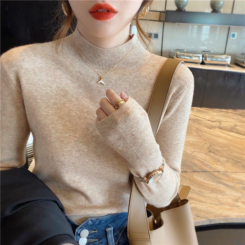 Frau in beigem Rollkragenpullover, goldene Halskette, rote Lippen, modisches Outfit.