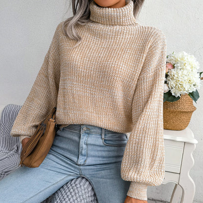 Frau in beigem Strickpullover mit Rollkragen, hellblauer Jeans, brauner Tasche, Blumen im Hintergrund.