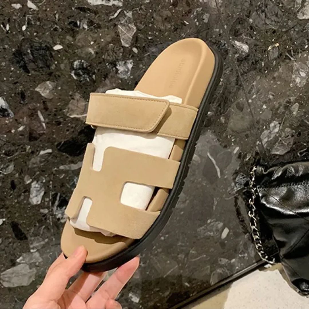 Beige Sandale mit Klettverschluss, schwarzer Sohle, auf Marmorboden, modisch und bequem.