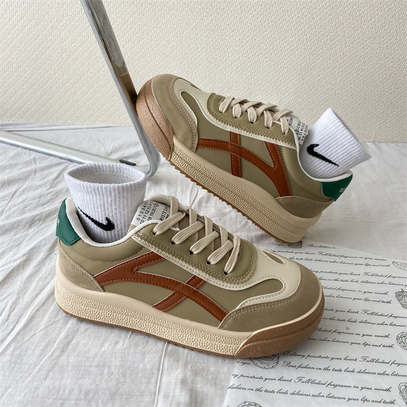 Beige Sneaker mit braunen Streifen, grüner Ferse, Nike-Socken, auf weißem Tuch.