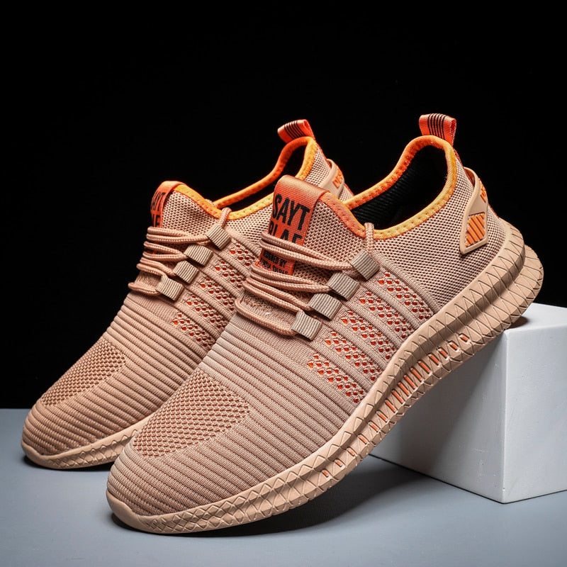 Beige Sportschuhe aus Mesh mit orangen Akzenten, rutschfeste Sohle, ideal für Laufen und Fitness.