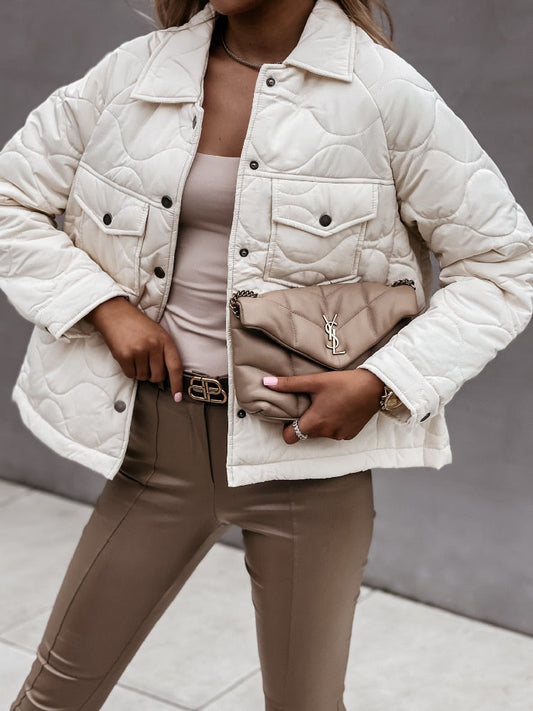 Frau in beiger Steppjacke mit Designer-Handtasche, beige Hose, modisches Outfit.