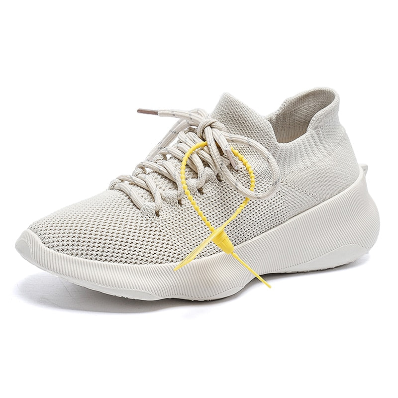 Beiger Sneaker aus Strickmaterial, atmungsaktiv, mit gelbem Akzent, ideal für Freizeit und Sport.