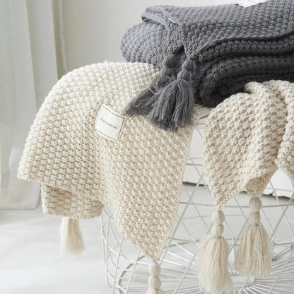 Beige und graue Strickdecken mit Quasten auf modernem Drahtkorb, gemütliche Wohnaccessoires.