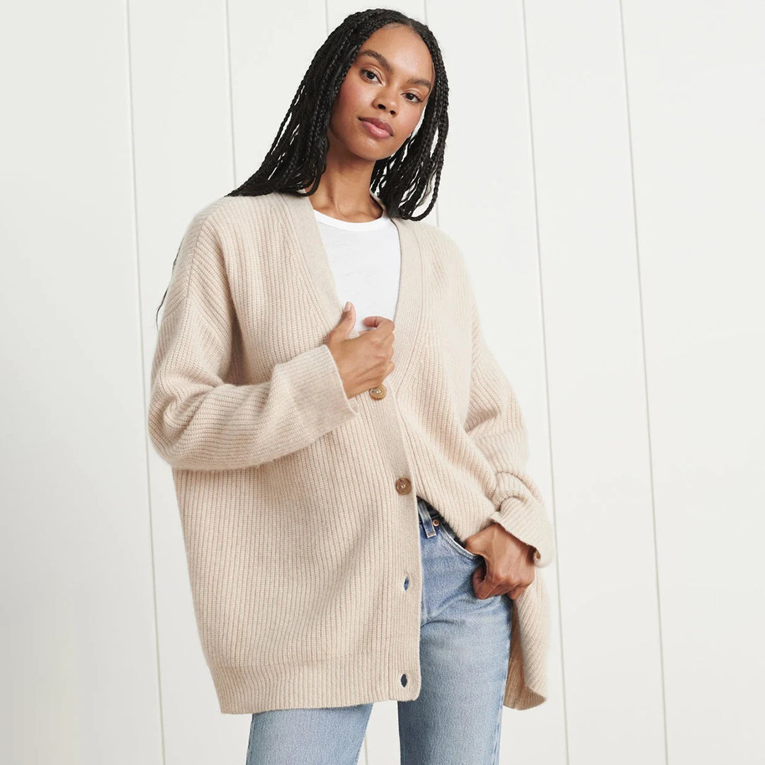 Frau trägt beige Strickjacke aus Wolle, lässig offen, über weißem T-Shirt und blauer Jeans.