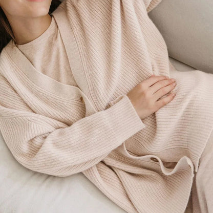Frau in beigem Strickcardigan auf Sofa, gemütliche Mode, weiches Material, lässiger Stil.