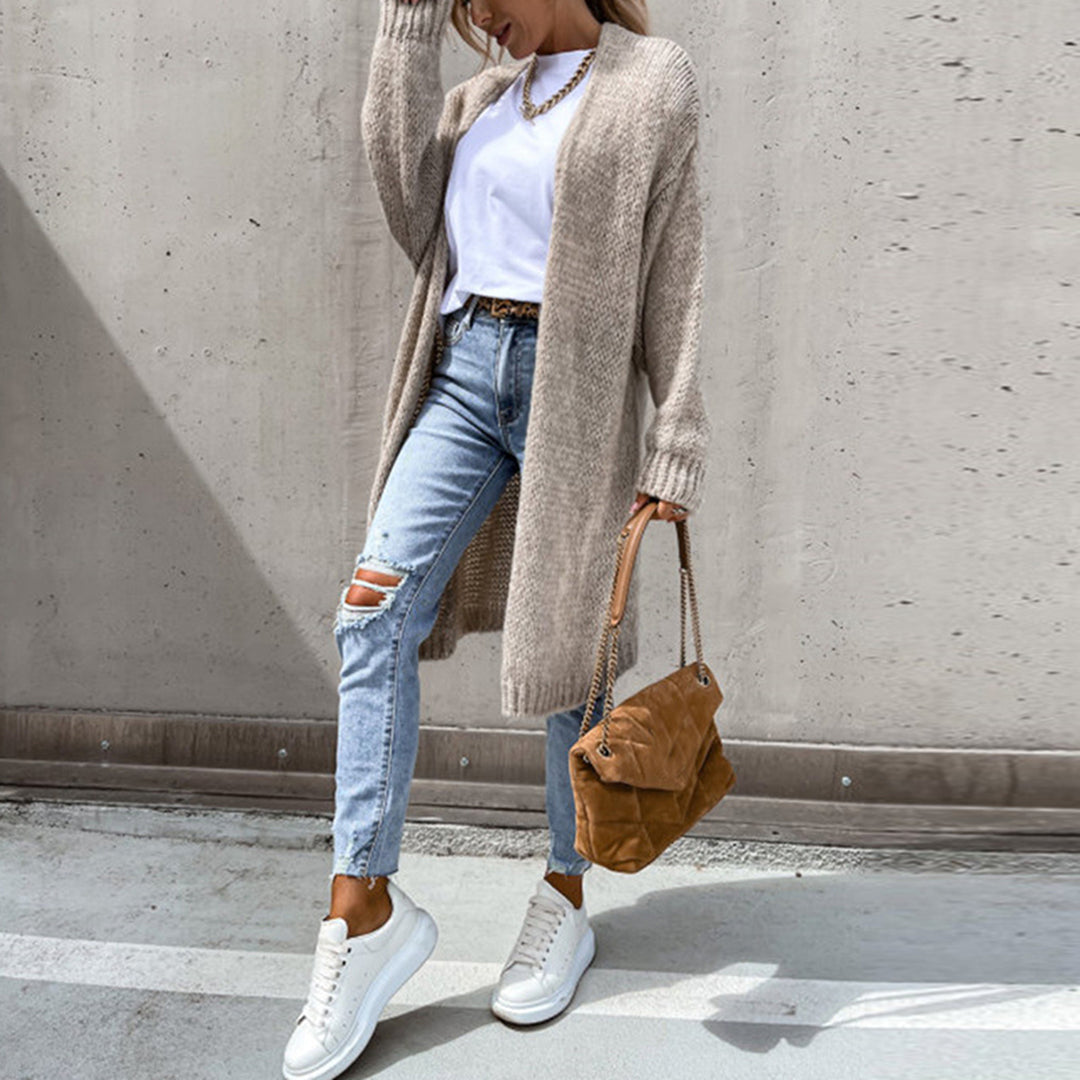 Frau in beigem Strickcardigan, weißem T-Shirt, zerrissenen Jeans und weißen Sneakers.
