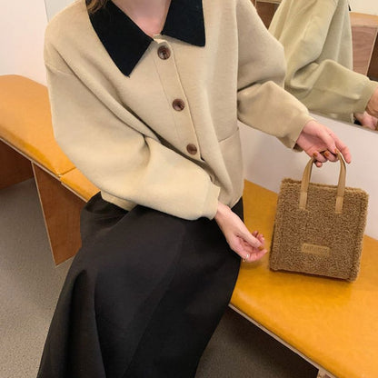 Frau mit beigem Wollmantel, schwarzem Kragen, braunem Knopf, brauner Tasche auf gelber Bank.