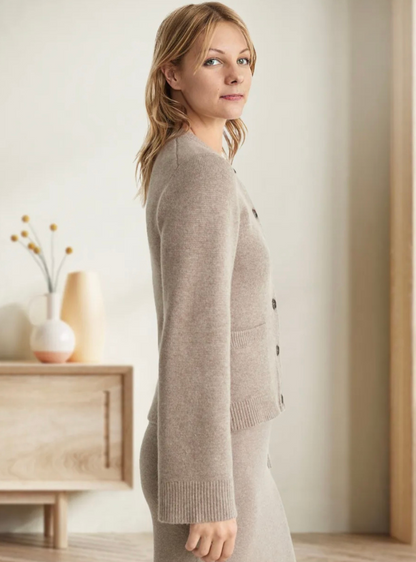Frau in beigem Strickpullover, stehend vor Holzmöbeln, moderne Inneneinrichtung.