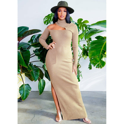 Frau in beige, schulterfreiem Strickkleid und Hut, vor grünen Pflanzen stehend.