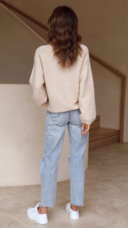 Frau in beiger Strickpullover und blauer Jeans, Rückansicht, modisch, lässiger Stil.