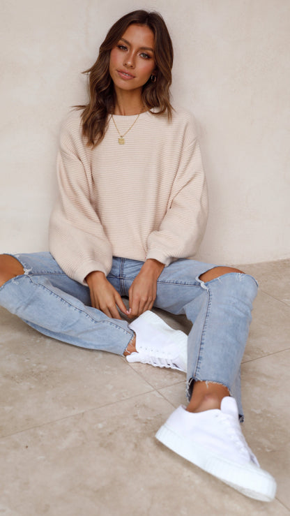 Frau in beigem Pullover und zerrissenen Jeans, weiße Sneaker, lässiger Look, Modefotografie.
