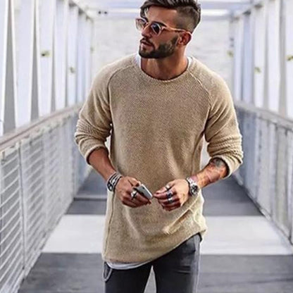 Mann mit beigem Strickpullover, Sonnenbrille und Armbändern auf Brücke.
