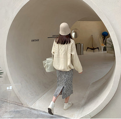 Frau in beigem Pullover und gemustertem Rock, beige Hut, weiße Tasche, Vintage-Mode.