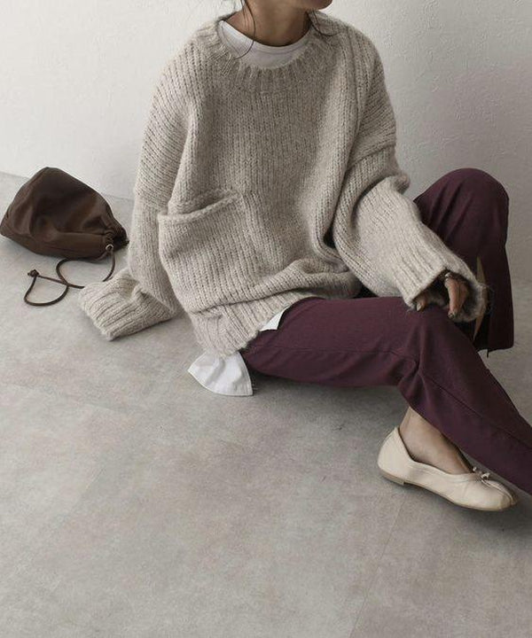 Frau in beigem Strickpullover, lila Hose, beigen Schuhen, braune Tasche, sitzt auf Boden.
