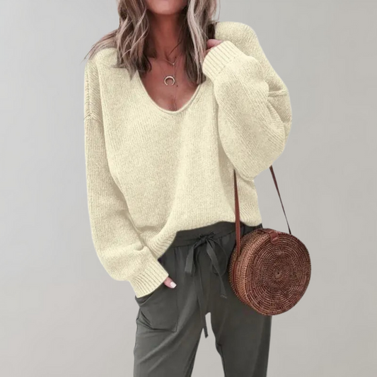 Frau in beigem Strickpullover, graue Hose, runde Strohtasche, modisch, lässiger Look.