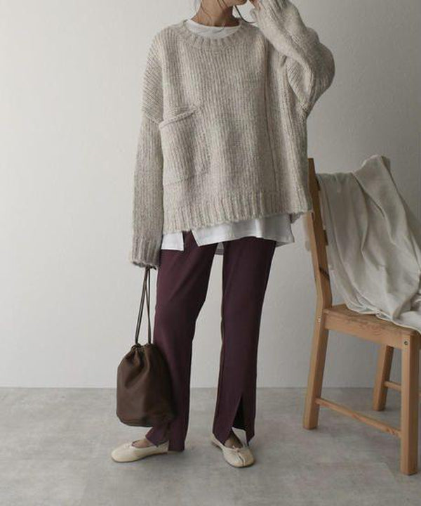 Person in beigem Strickpullover, weißem Shirt, brauner Hose, Halbschuhen, mit brauner Tasche.