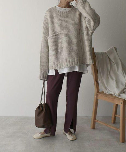 Person in beigem Strickpullover, weißem Shirt, brauner Hose, Halbschuhen, mit brauner Tasche.