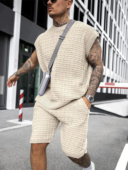 Mann in beigem Strick-Set, ärmelloses Oberteil und Shorts, modisch, urbaner Stil.