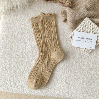 Beige Wollsocken mit Zopfmuster auf weißem Hintergrund, gemütlich, warm, Strickmode.