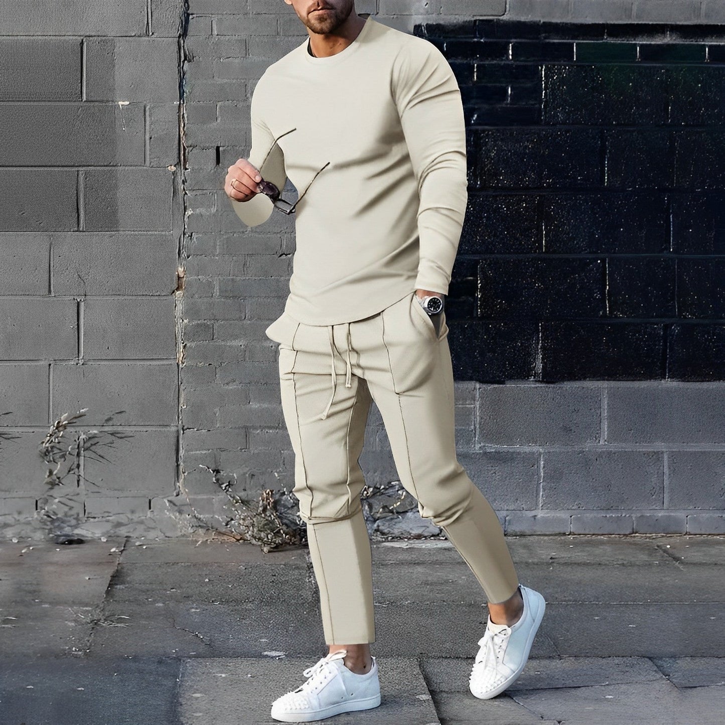 Mann in beigem Trainingsanzug, weiße Sneaker, graue Wand, urbane Mode, Streetwear-Look.