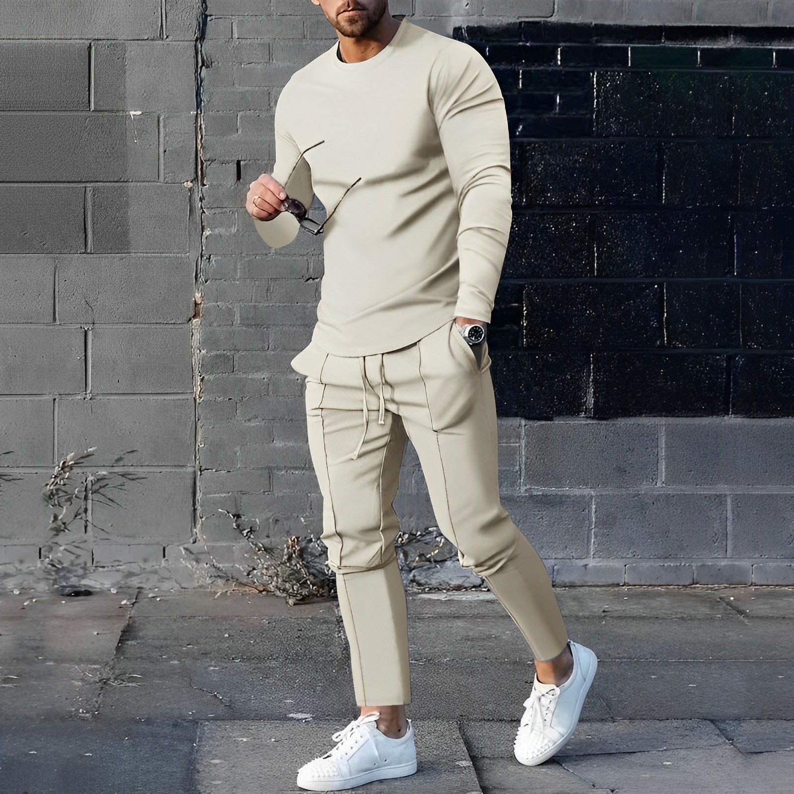 Mann in beigem Trainingsanzug, weiße Sneaker, graue Wand, urbane Mode, Streetwear-Look.