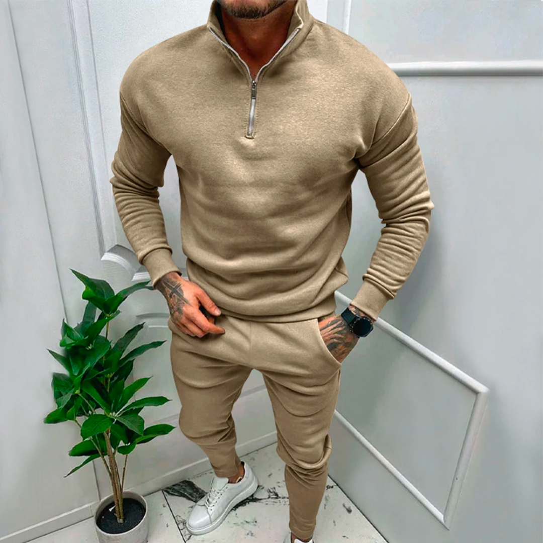 Mann in beigem Jogginganzug mit Reißverschluss, moderne Freizeitmode, Indoor-Pflanze, weiße Sneaker.