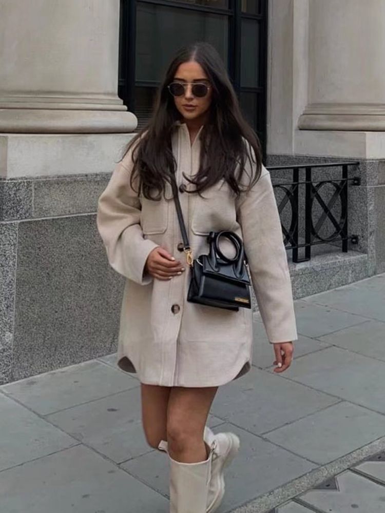 Frau in beigem Wollmantel, schwarze Tasche, Sonnenbrille, weiße Stiefel, Stadtstraße.