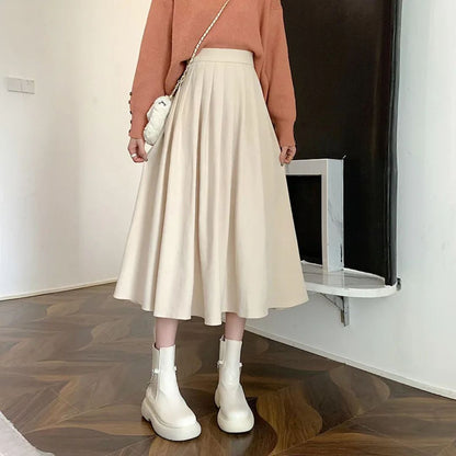 Damenmode: Beiger Faltenrock, weißer Pullover, weiße Stiefel, eleganter Herbst-Look.