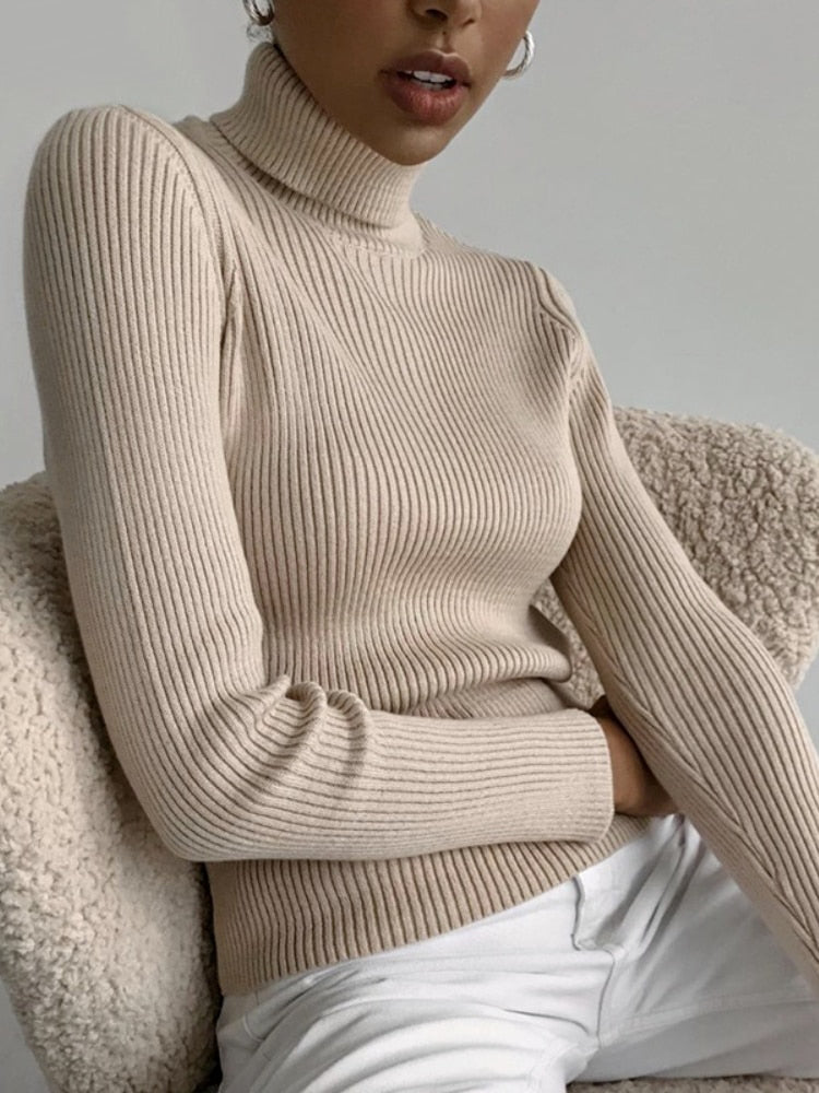 Frau trägt beige Rollkragenpullover aus Strick, sitzt auf beigem Sessel, modisch, elegant.