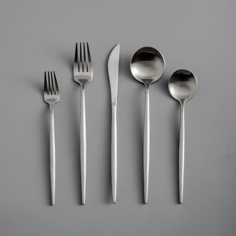 Fünfteilige Edelstahl-Besteckset, bestehend aus Gabeln, Messer, Löffeln auf grauem Hintergrund.