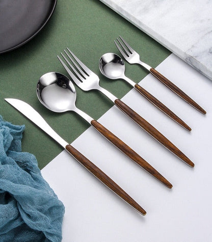 Besteckset aus Edelstahl mit Holzgriffen, bestehend aus Messer, Gabeln und Löffeln auf Tisch.